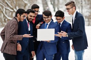 Group of six indian businessman in suits posed outdoor in winter day at Europe, looking on laptop.